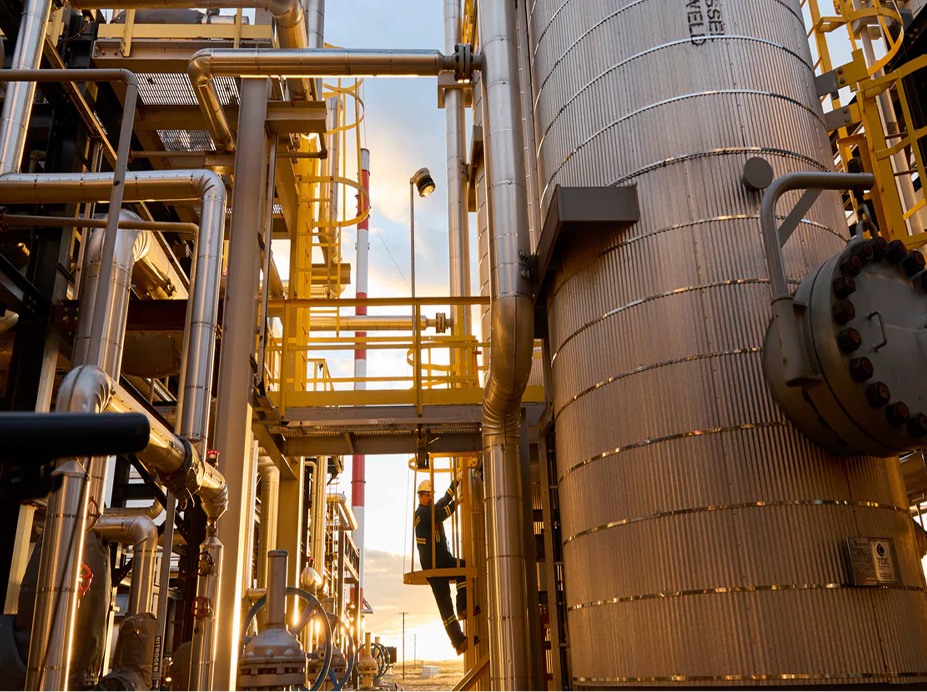 Industrial site with piping, platforms, and a worker in safety gear