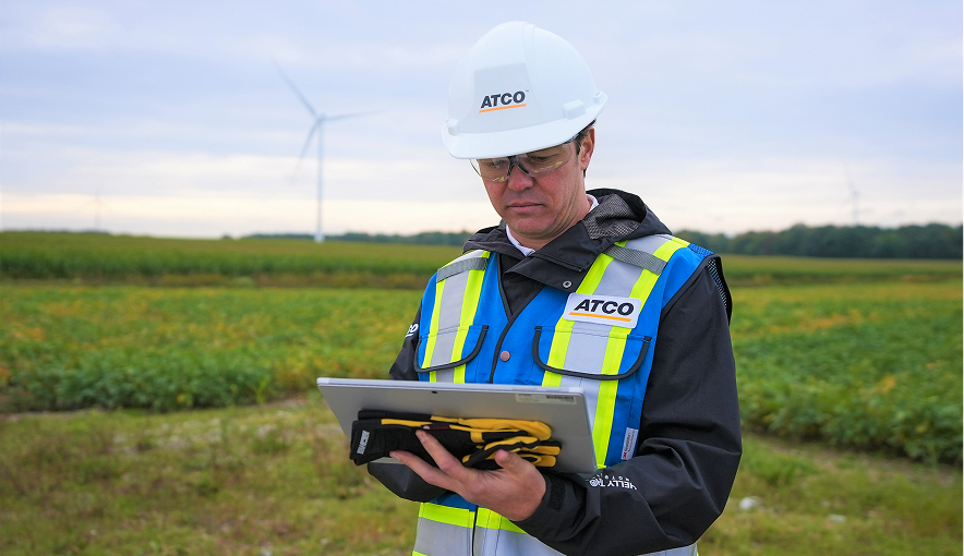 Worker using a tablet in a field with wind turbines