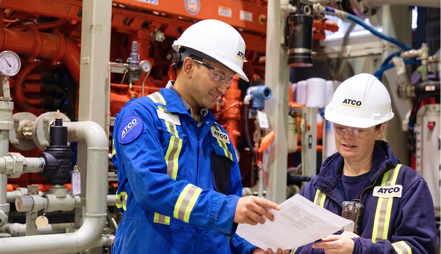 Two ATCO workers reviewing documents in an industrial facility